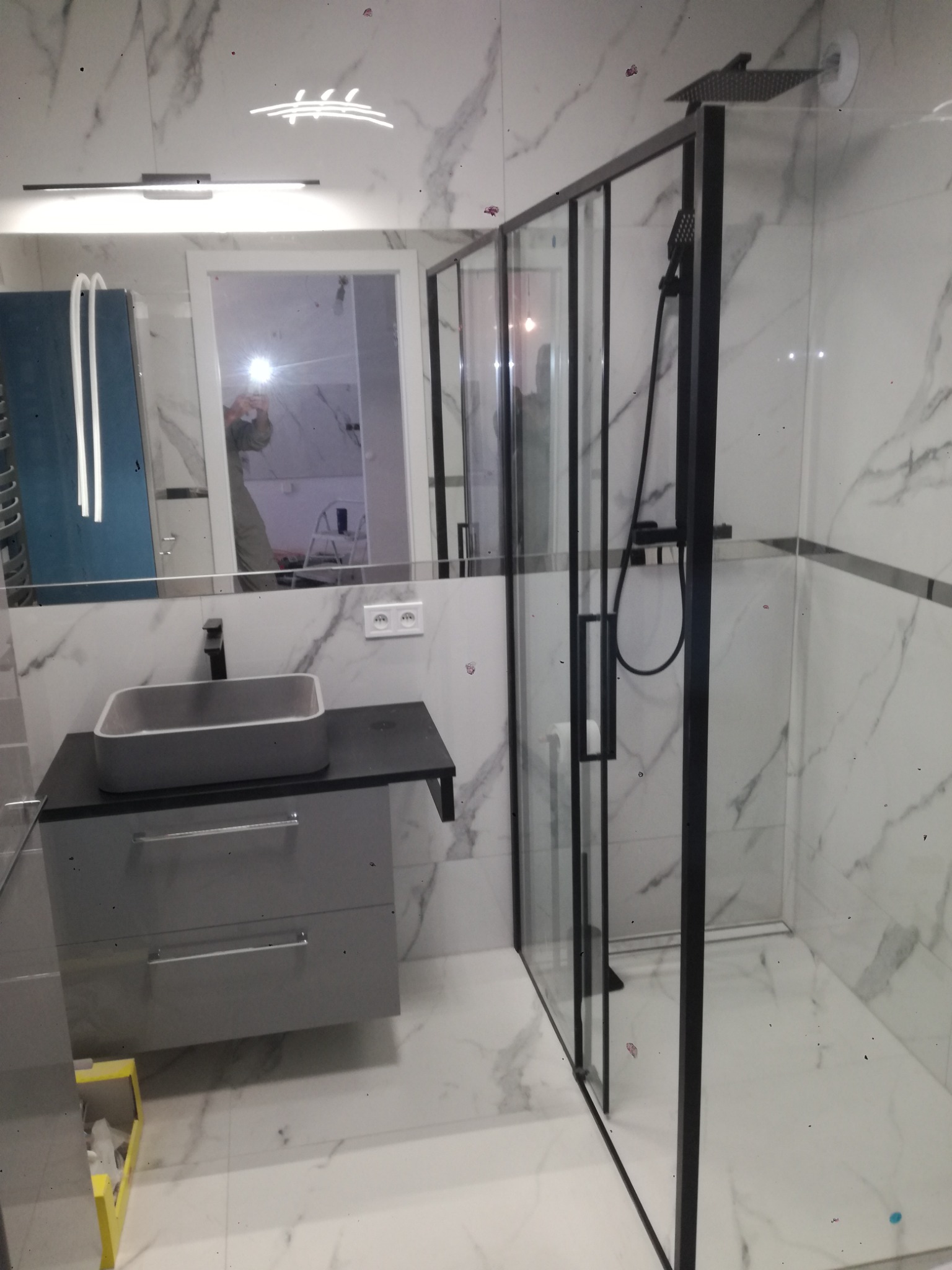 Nowoczesna łazienka w Kołobrzegu z kabiną prysznicową typu walk-in z czarnymi profilami, umywalką nablatową w odcieniach szarości i marmurowymi płytkami na ścianach.