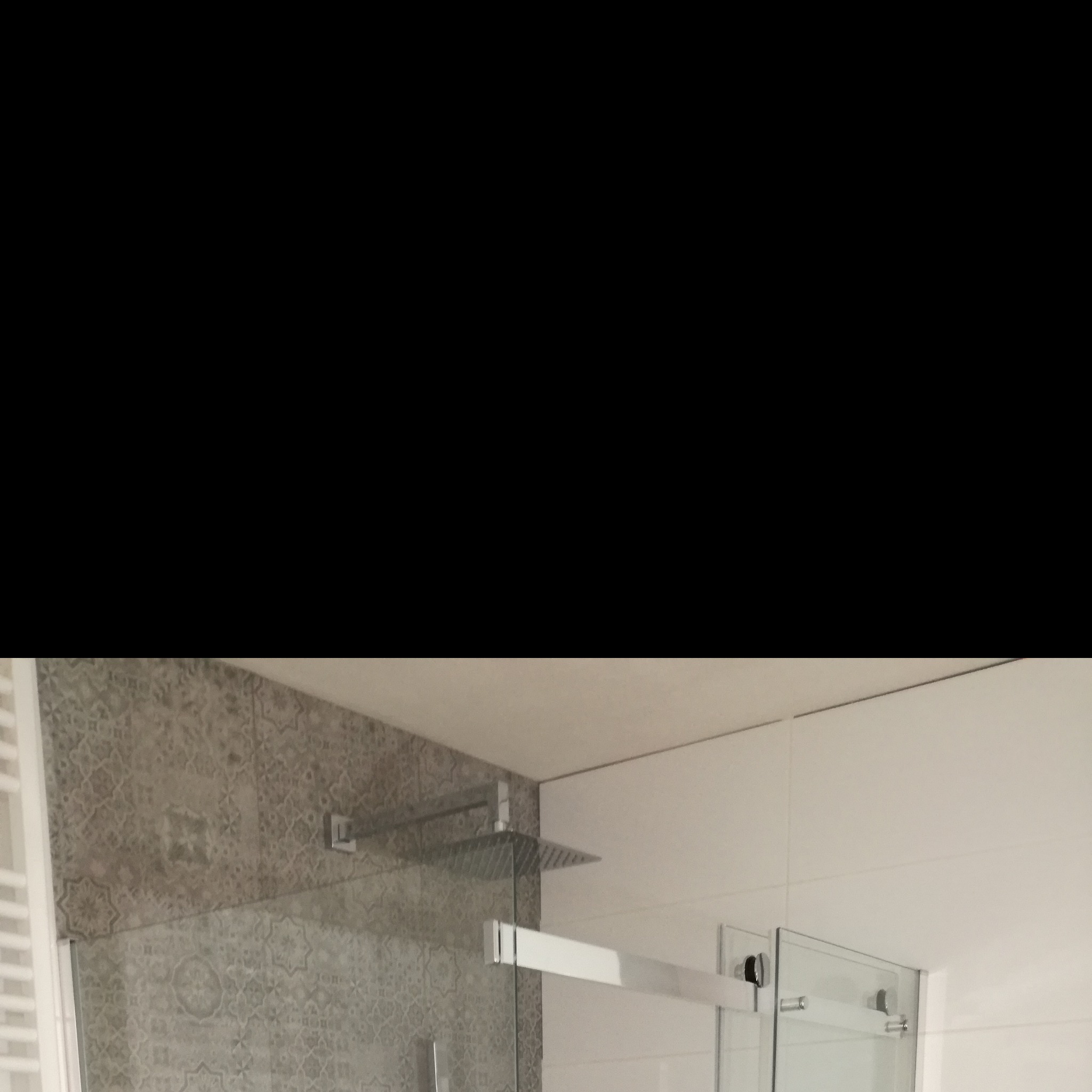 Nowoczesna kabina prysznicowa z deszczownicą i szklanymi drzwiami, obok ściana wyłożona płytkami z wzorem marokańskim, a po prawej białe, gładkie płytki.