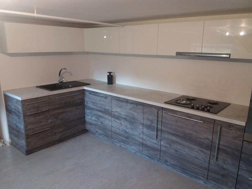 Nowoczesna kuchnia z szarymi szafkami imitującymi drewno i białymi szafkami wiszącymi, czarny zlew i płyta grzewcza, minimalistyczny design.