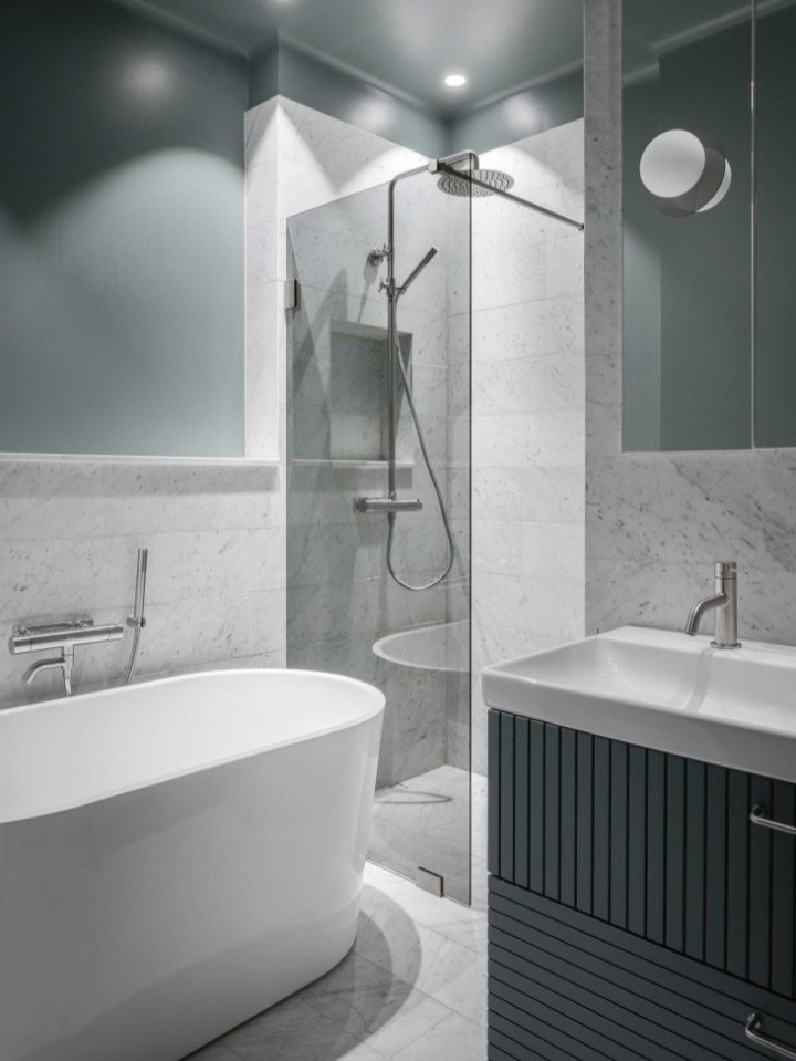 Nowoczesna łazienka z wanną wolnostojącą, kabiną prysznicową typu walk-in i umywalką z szafką w odcieniach szarości, wykończona marmurem.