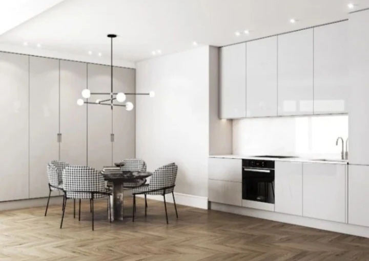 Nowoczesna kuchnia z białymi, lakierowanymi frontami, drewnianą podłogą w jodełkę i okrągłym stołem z krzesłami w pepitkę pod designerską lampą.