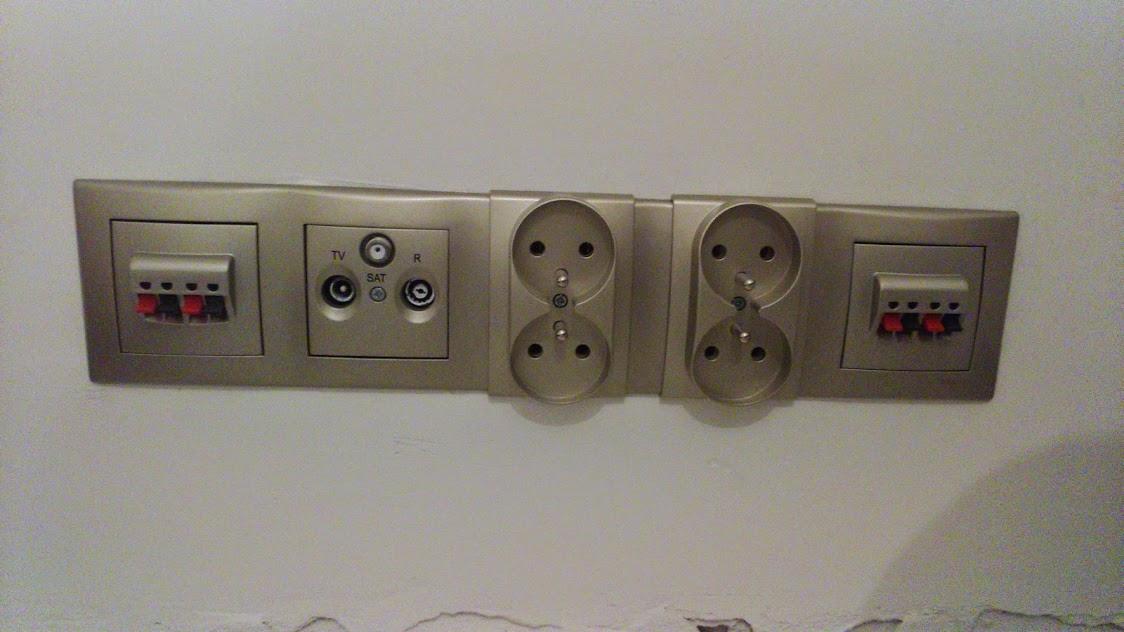 Zestaw gniazd elektrycznych i antenowych w kolorze szampańskim, zamontowany na ścianie z widocznymi śladami po remoncie.