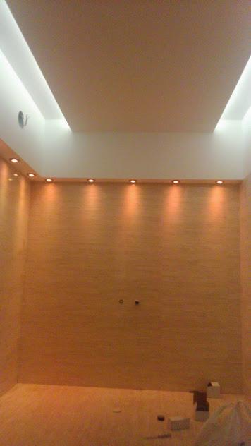 Pokój z oświetleniem LED w suficie podwieszanym i punktowym oświetleniem ściennym, widoczne puszki instalacyjne na ścianie.