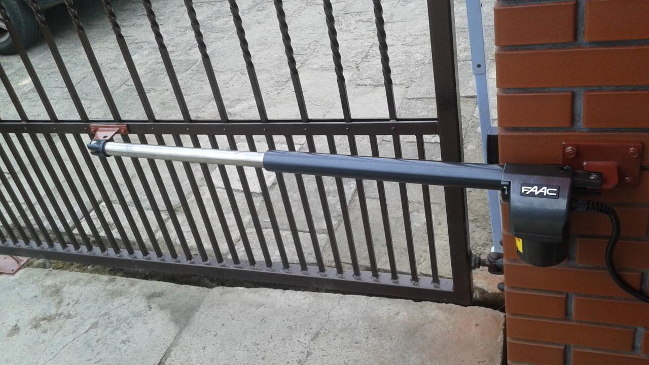 Automatyka bramy skrzydłowej FAAC zamontowana na murowanym słupku z czerwonej cegły, widoczne ramię siłownika i fragment metalowej bramy.