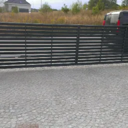 Automatyczna brama wjazdowa z poziomymi panelami, zamontowana między murowanymi słupkami, z kostką brukową na podjeździe i widocznym mechanizmem otwierającym.