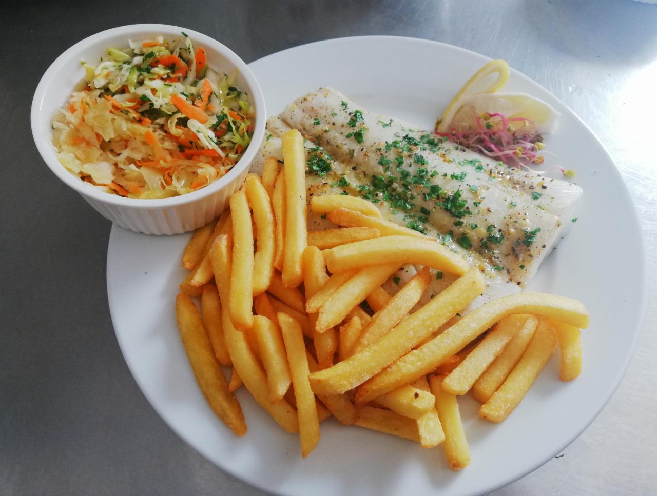 Porcja smażonej ryby z frytkami i surówką z kapusty, udekorowana cytryną i kiełkami na białym talerzu.
