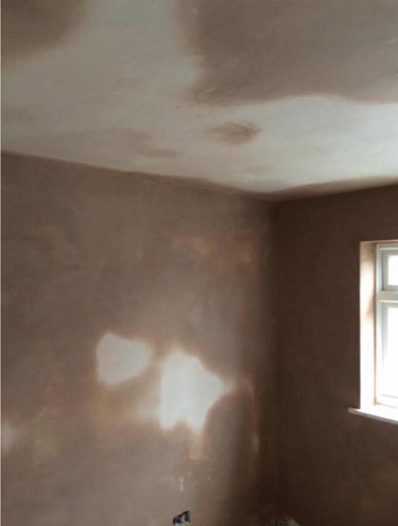 Świeżo otynkowane ściany i sufit w pokoju, widoczne nierówności na powierzchni, przygotowanie do malowania, okno z białymi ramami po prawej stronie.