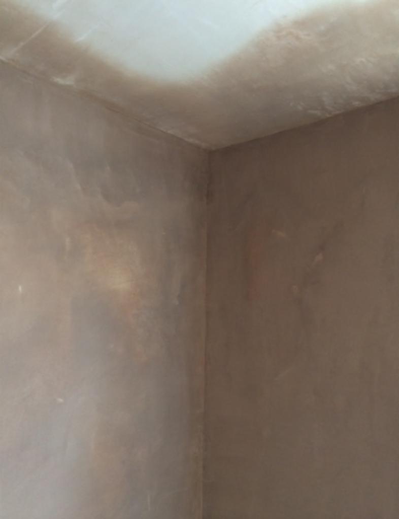 Wnętrze pomieszczenia po tynkowaniu, widoczne świeże, nierównomiernie wyschnięte tynki na ścianach i suficie, z delikatnymi smugami i różnicami w odcieniach szarości.