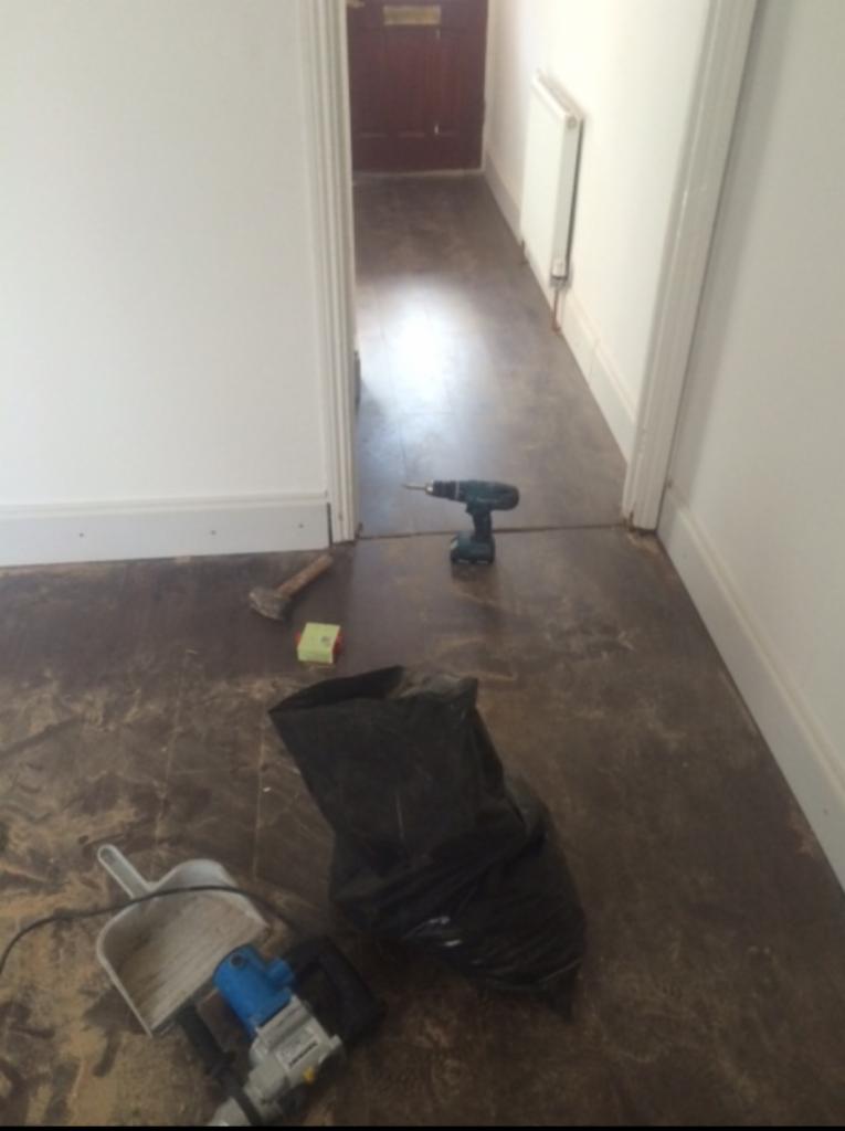 Przygotowania do remontu podłogi w korytarzu: wiertarka, młotek, szpachelka, worek na śmieci i pozostałości po starej podłodze.