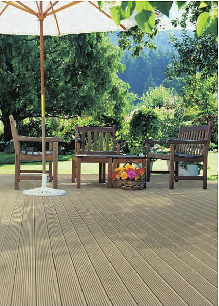 Kompozytowa deska tarasowa w odcieniach beżu, ułożona na zewnątrz, z drewnianymi krzesłami i stolikiem pod parasolem ogrodowym, na tle zieleni.