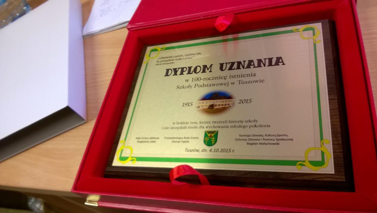 Dyplom uznania w czerwonym pudełku, upamiętniający 100-lecie Szkoły Podstawowej w Tuszowie, z datami 1915-2015 i podpisami przedstawicieli gminy.