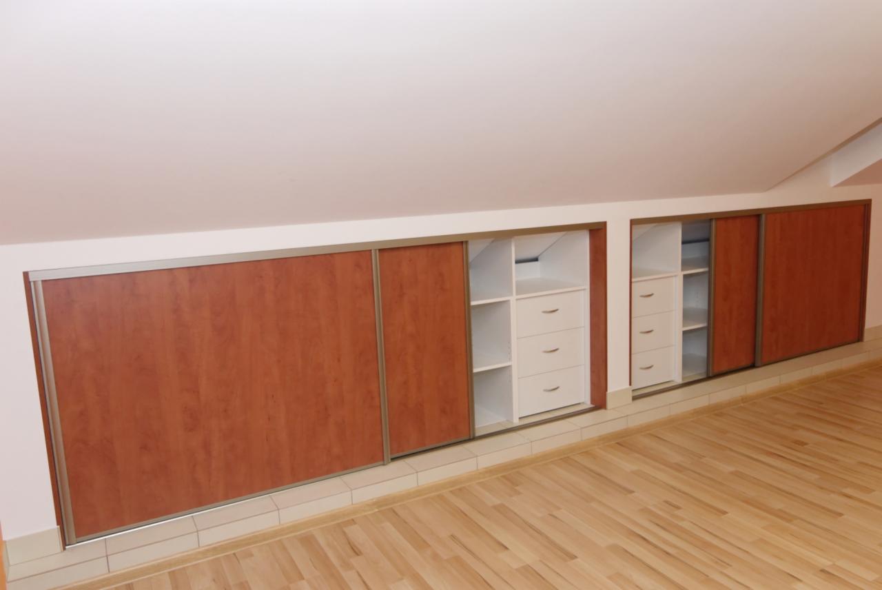 Zabudowa wnęki na poddaszu ze skośnym sufitem, z przesuwnymi drzwiami z okleiną drewnopodobną i białymi regałami z szufladami.