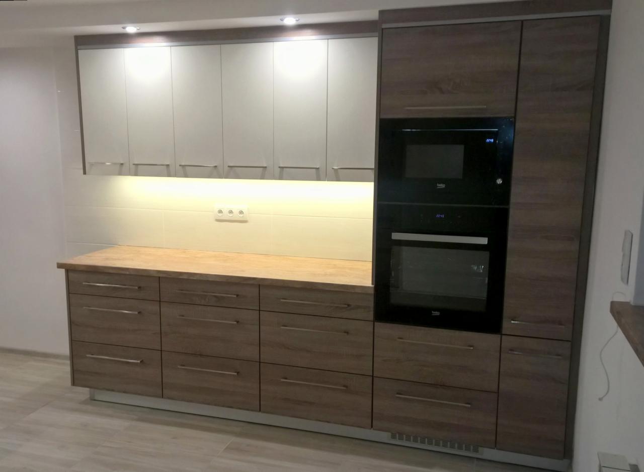 Nowoczesna kuchnia z szarymi szafkami wiszącymi, drewnopodobnymi szafkami dolnymi z szufladami i zabudowanym piekarnikiem oraz mikrofalówką marki Beko.