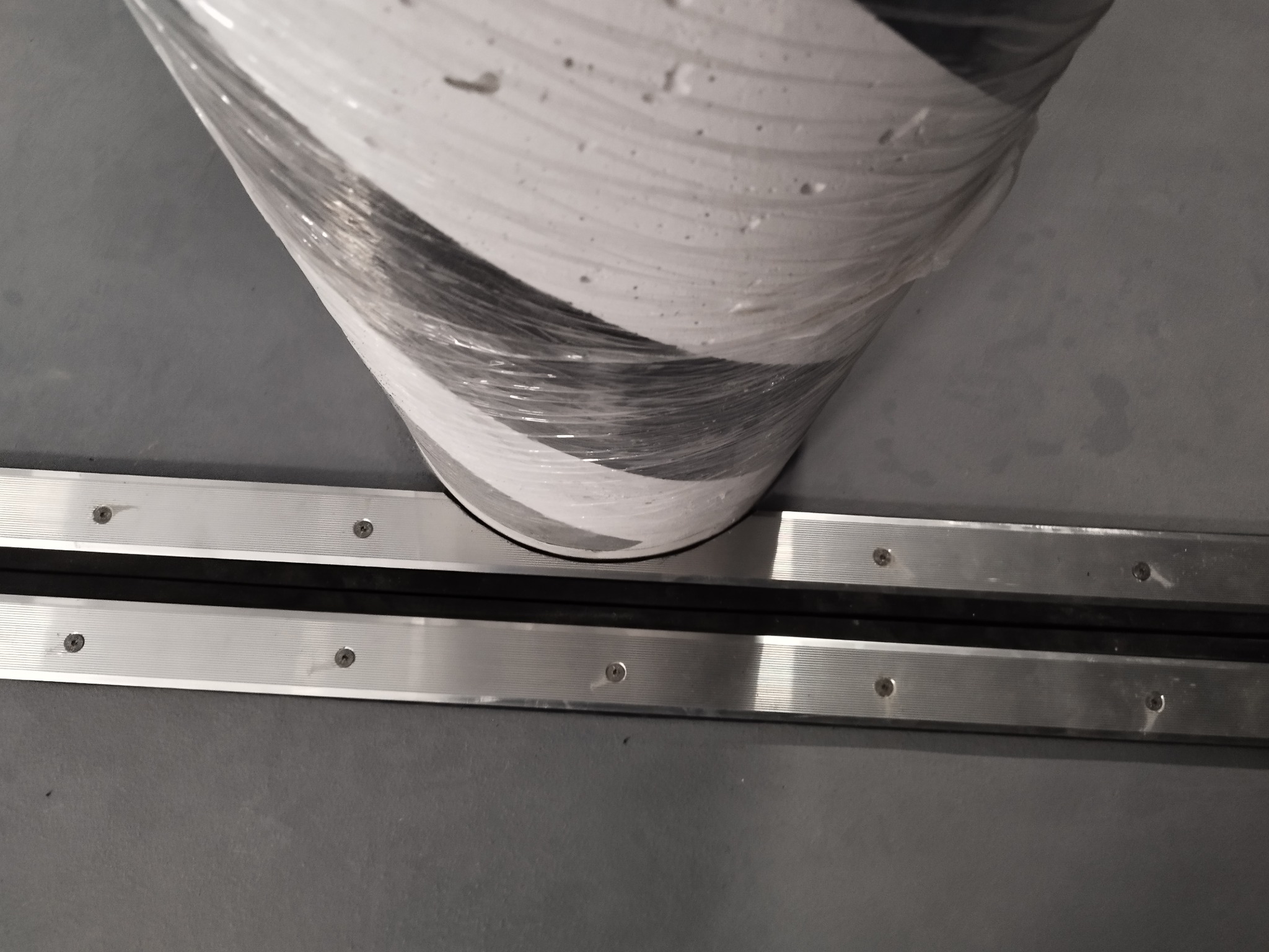 Oznakowany, owinięty folią ochronną słup na szarej podłodze przemysłowej z dylatacją aluminiową.