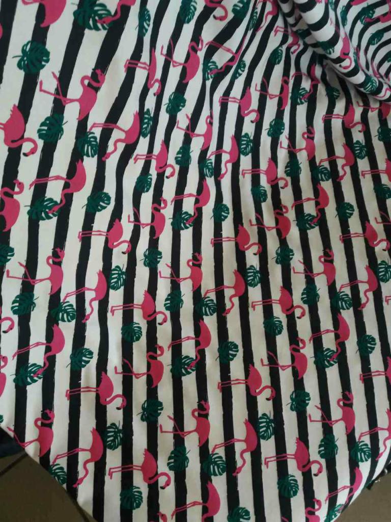Tkanina w biało-czarne pasy z motywem różowych flamingów i zielonych liści monstery.