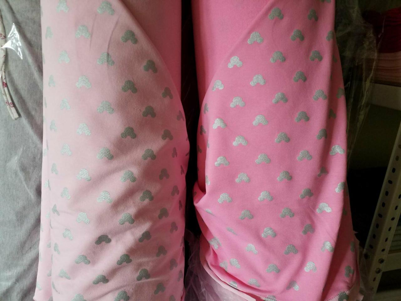 Dwa wałki różowej tkaniny z nadrukiem w srebrne chmurki, jeden w jaśniejszym odcieniu różu, ułożone obok siebie.