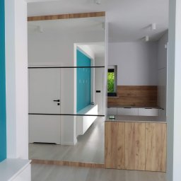 MEBLE XY NORBERT BOGDANOW - Nowoczesna zabudowa przedpokoju z lustrem, łącząca szafę i siedzisko w bieli i drewnie. Akcent turkusowej ściany dodaje świeżości wnętrzu.