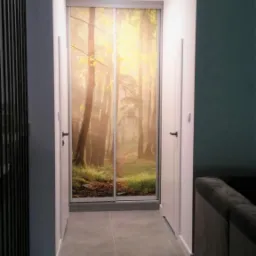 Korytarz z szarą podłogą i szafą wnękową z przesuwnymi drzwiami z fototapetą przedstawiającą leśny krajobraz.