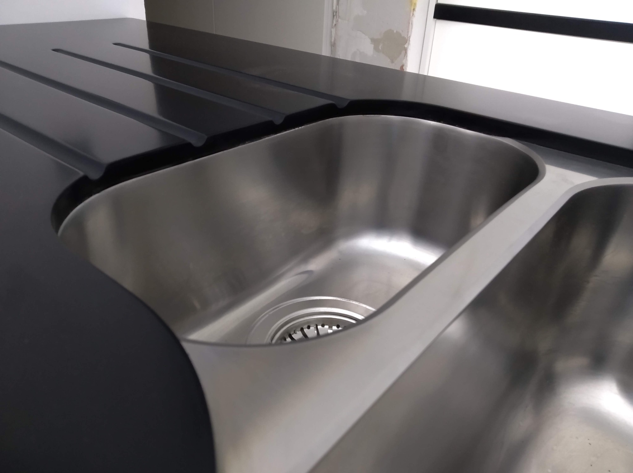 Nowoczesny, dwukomorowy zlew ze stali nierdzewnej, wkomponowany w czarny, gładki blat z ociekaczem. Minimalistyczny design, jasne tło.