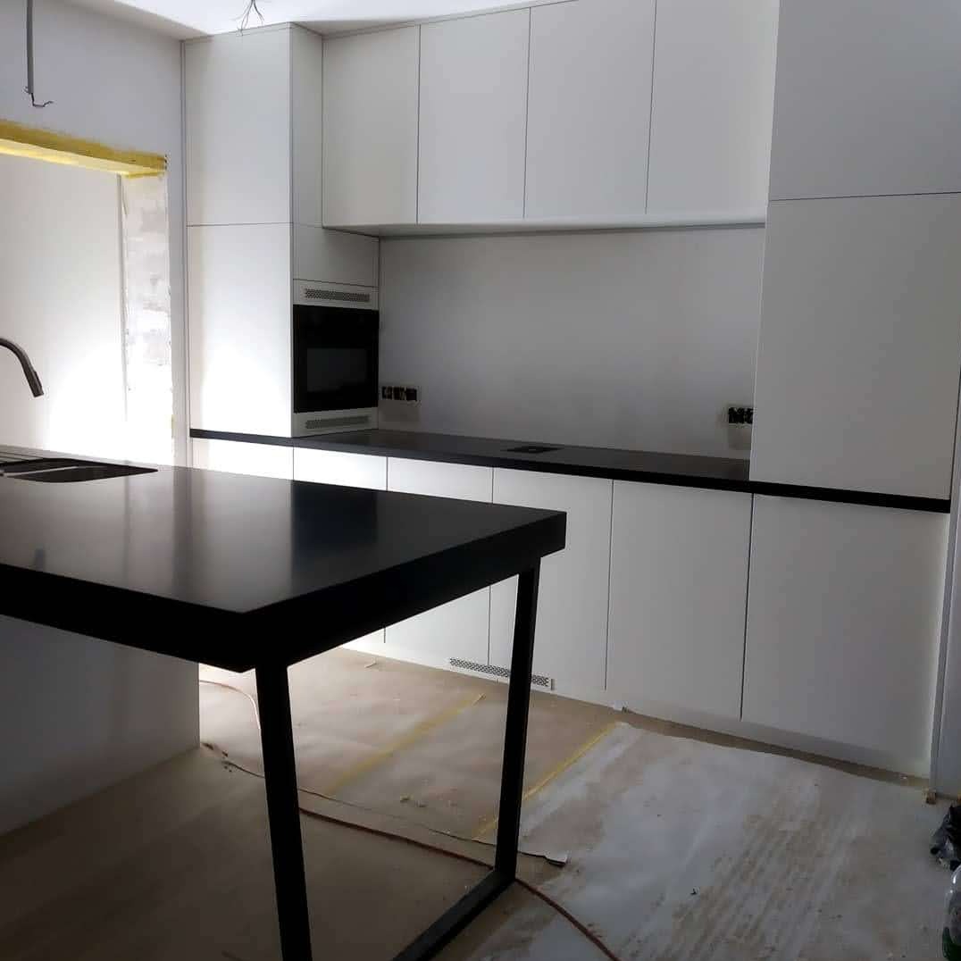 Biała kuchnia z czarnym blatem w trakcie montażu. Widoczne niedokończone ściany i podłoga. Minimalistyczny design, nowoczesne wykończenie.