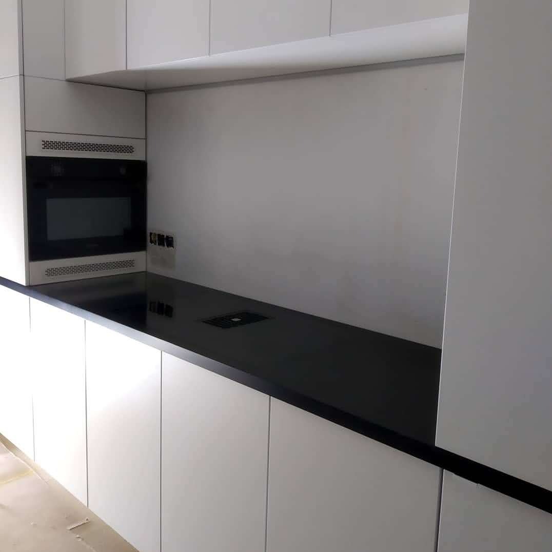 Minimalistyczna kuchnia: białe szafki z czarnym blatem, wbudowany piekarnik i gniazdko w blacie. Nowoczesny design, stonowana kolorystyka, proste linie.