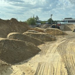 SZWAGIER-KOP SPÓŁKA Z OGRANICZONĄ ODPOWIEDZIALNOŚCIĄ - Kopalnia piasku z hałdami i śladami opon ciężkiego sprzętu. W tle budynki i błękitne niebo z chmurami, widok z kabiny pojazdu.