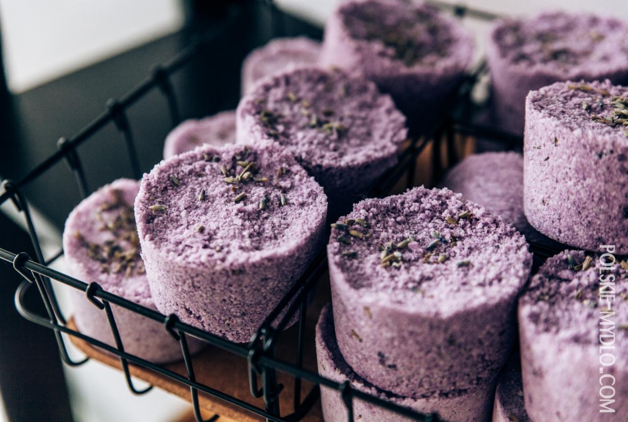 Fioletowe, okrągłe mydła lawendowe w czarnym, drucianym koszyku, posypane suszoną lawendą, widoczne z bliska w naturalnym świetle.