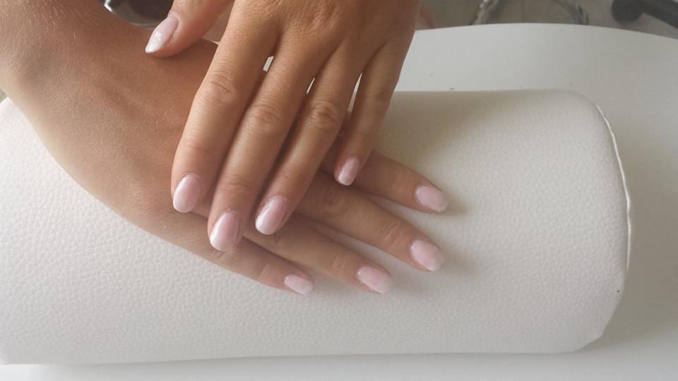 Delikatny, jasnoróżowy manicure z efektem ombre na krótkich paznokciach, wykonany w Tomaszowie Mazowieckim, na tle białego podkładu pod dłonie.