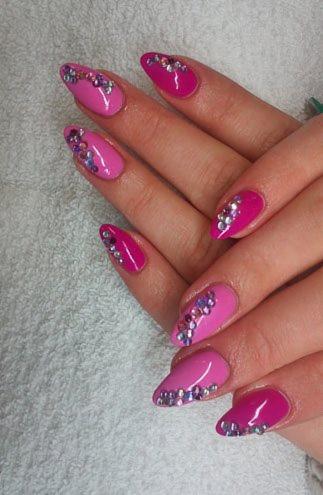 Różowe, migdałowe paznokcie zdobione drobnymi, połyskującymi kryształkami na tle białego ręcznika.