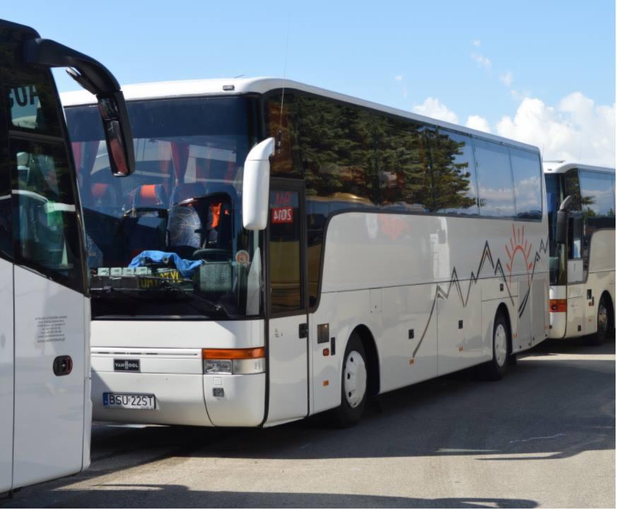 Biały autokar z grafiką gór i słońca na boku, zaparkowany obok innych autokarów, widoczny numer rejestracyjny.