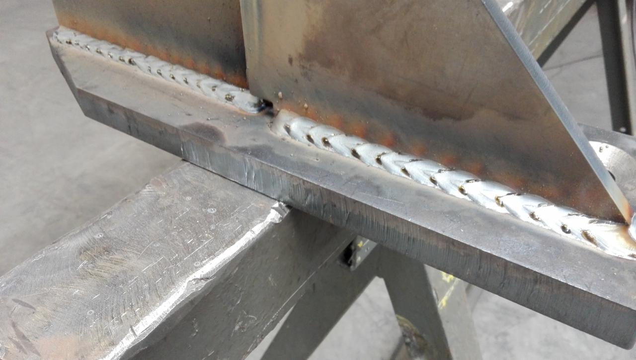 Szczegółowe ujęcie spawu łączącego metalowe elementy konstrukcyjne, widoczne ślady obróbki i surowy wygląd materiałów.