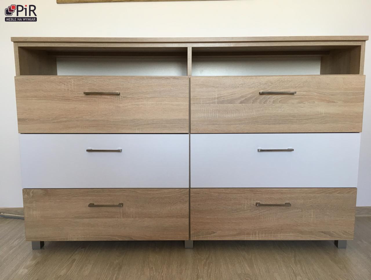 Komoda z sześcioma szufladami w trzech rzędach, z frontami w kolorze drewna i białym, z metalowymi uchwytami, stojąca na metalowych nóżkach.