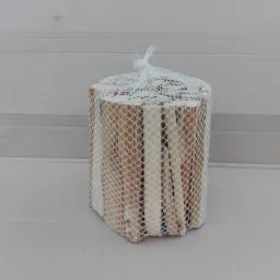 Siatka z drobnymi, suchymi kawałkami drewna, idealnymi na rozpałkę do kominka, ułożona na szarym kartonie.