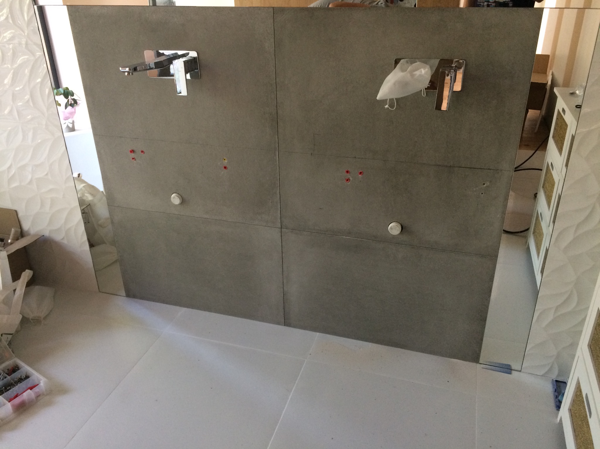 Montaż szarej ściany z płytek w łazience z chromowaną armaturą i widocznymi otworami montażowymi oraz narzędziami w tle.