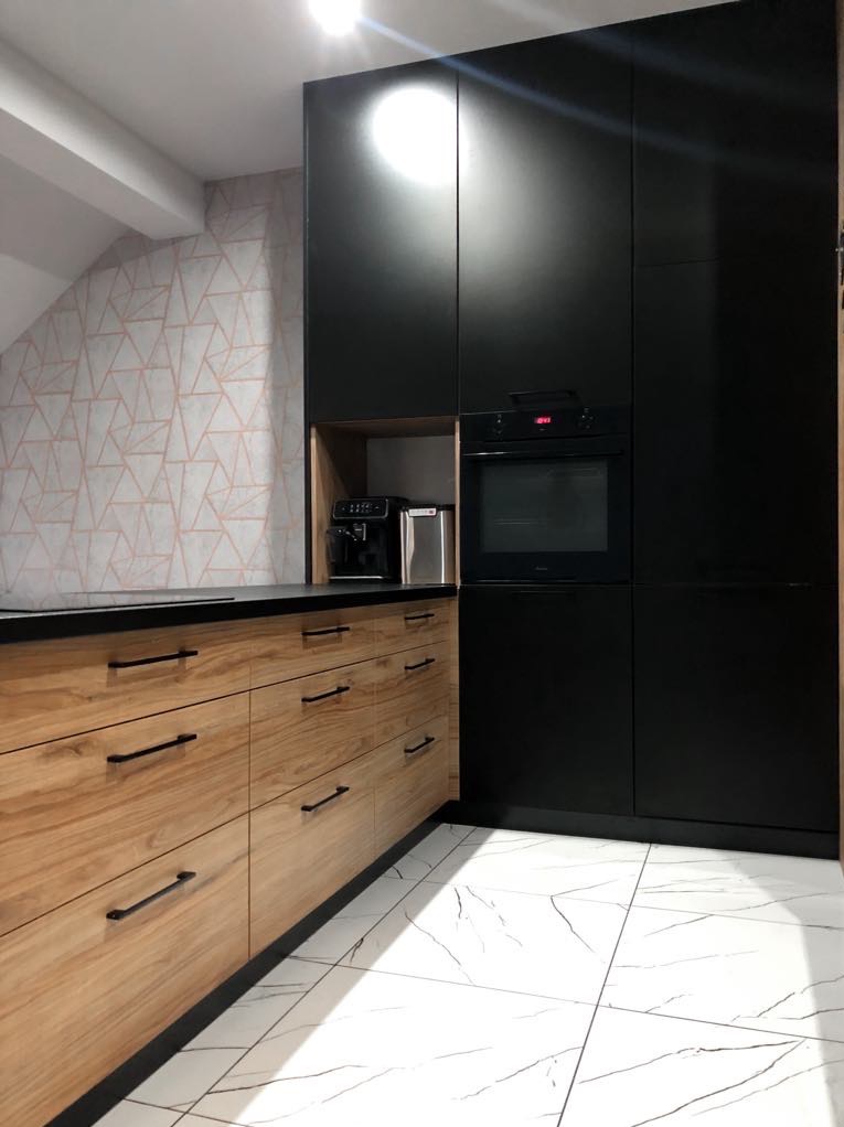Nowoczesna kuchnia: połączenie drewnianych frontów z czarnymi szafkami, czarny blat, marmurowe płytki podłogowe i geometryczna tapeta w tle.