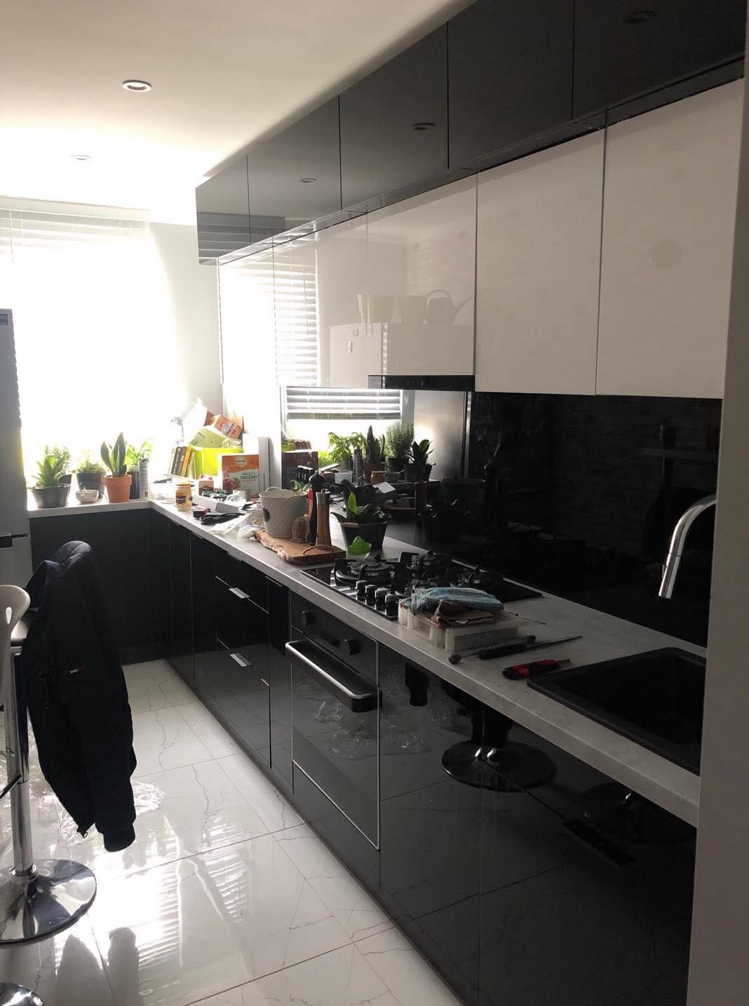 Nowoczesna kuchnia w trakcie montażu: czarne, lakierowane fronty szafek dolnych, białe szafki górne, blat roboczy z narzędziami, widoczne rośliny doniczkowe na blacie przy oknie.