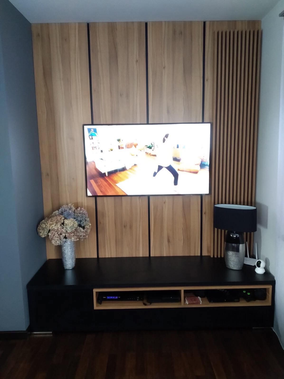 Drewniana zabudowa ściany z telewizorem i szafką RTV w Jaczowie, z dekoracyjnymi lamelami po prawej stronie.