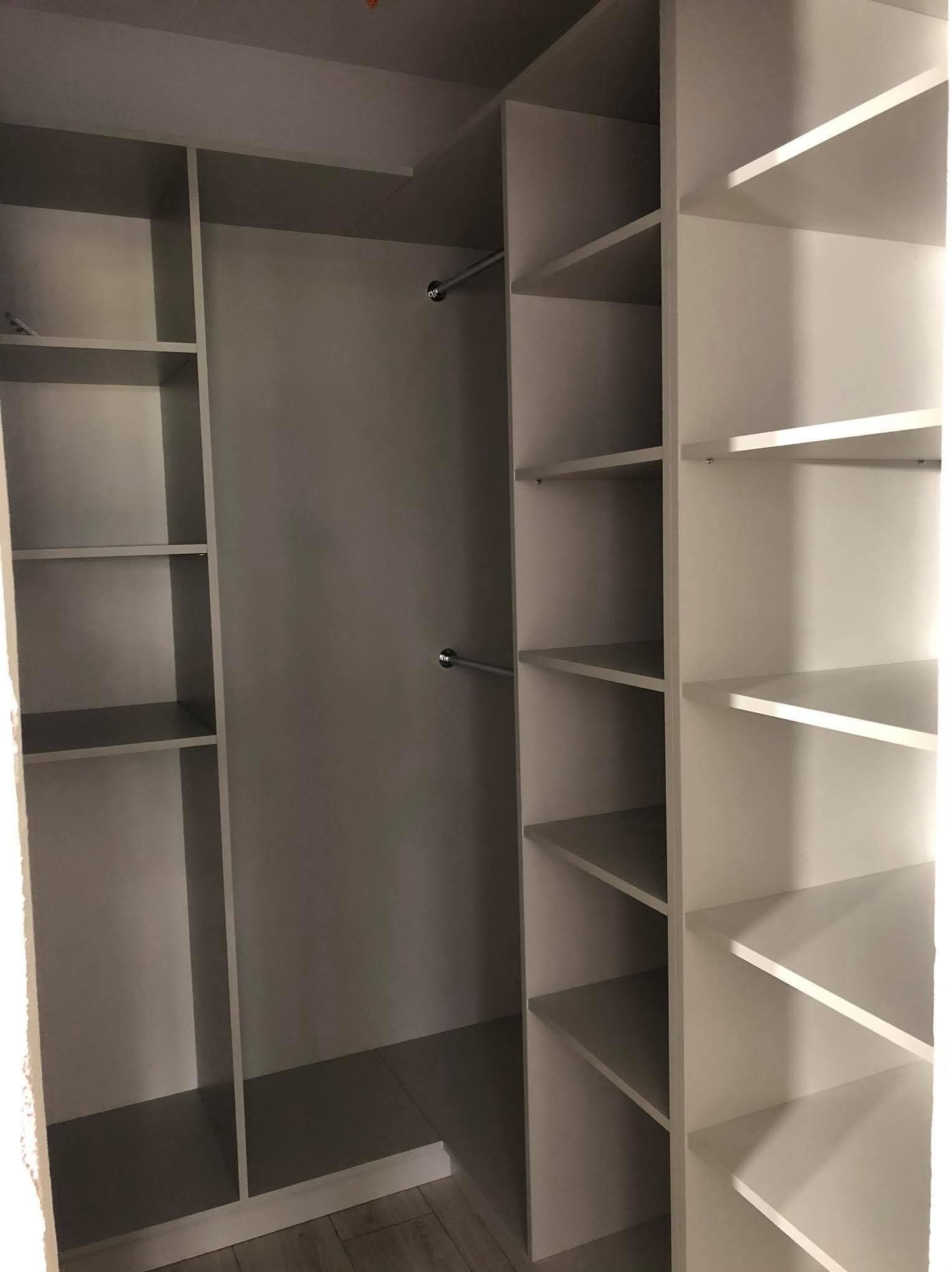 Wnętrze szafy z półkami i drążkami na ubrania, w odcieniach bieli i szarości, widok z perspektywy wnętrza pomieszczenia.