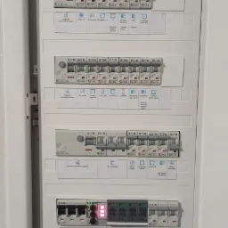 Otwarta skrzynka bezpiecznikowa z wyłącznikami różnicowoprądowymi i bezpiecznikami automatycznymi Eaton, opisana nazwami obwodów, z diodami sygnalizacyjnymi stanu. Widoczne oznaczenia obwodów...