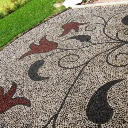 Ułożona kostka brukowa z dekoracyjnym wzorem roślinnym w kolorach brązowym i czarnym, na tle zielonego trawnika.