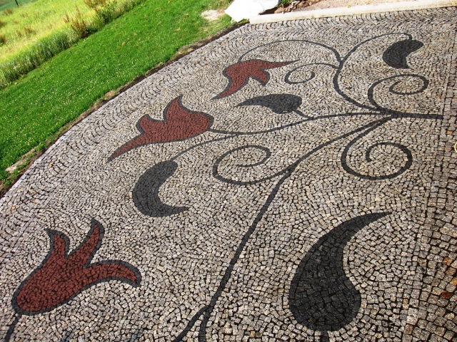 Ułożona kostka brukowa z dekoracyjnym wzorem roślinnym w kolorach brązowym i czarnym, na tle zielonego trawnika.