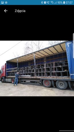 Ciężarówka z otwartą plandeką załadowana metalowymi elementami konstrukcyjnymi w kształcie kwadratów, mężczyzna na zewnątrz przytrzymuje jeden z elementów.