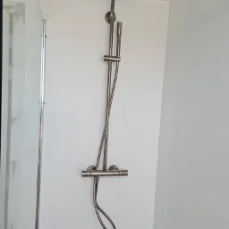 Zamontowany panel prysznicowy z deszczownicą i termostatem w nowoczesnej kabinie prysznicowej z białymi ścianami.