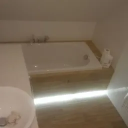 Wykończona łazienka na poddaszu w Dobczycach z wanną, umywalką i grzejnikiem drabinkowym. Uwagę zwraca podświetlenie pod wanną.