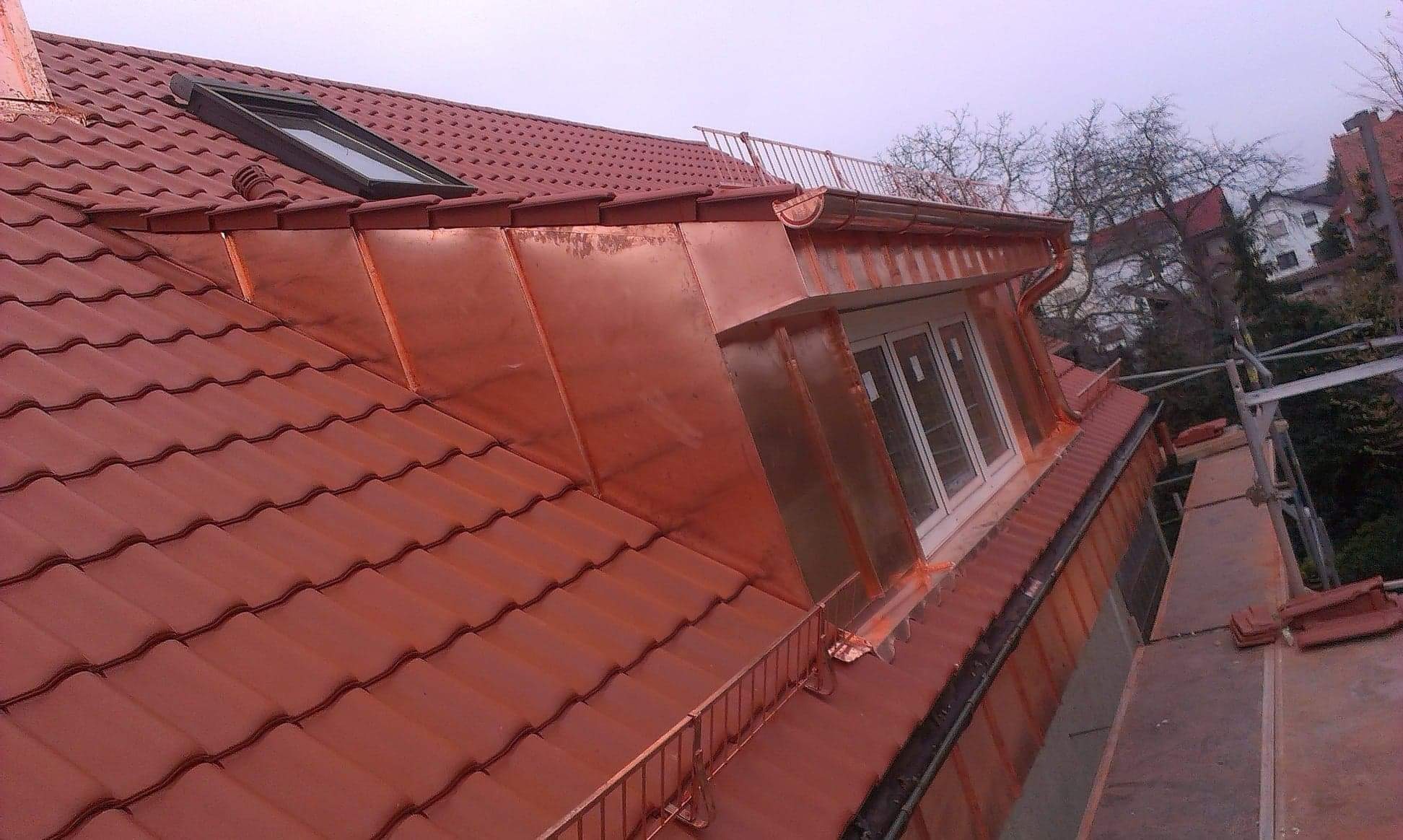 Czerwony dach z dachówką ceramiczną, okno dachowe i miedzianą obróbką blacharską lukarny, widok z rusztowania.