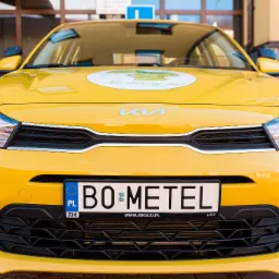 Żółty samochód z naklejką 'Nie stresuj się!' na masce, tablica rejestracyjna 'BO METEL', przód pojazdu.