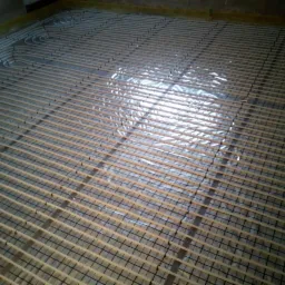 Rozłożona instalacja ogrzewania podłogowego z rurkami na folii refleksyjnej, widok z góry.