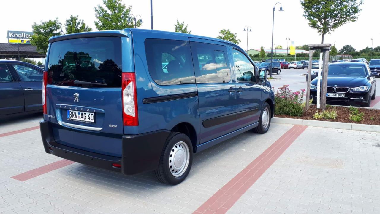 Niebieski bus Peugeot Expert Tepee zaparkowany na parkingu z kostki brukowej, widoczny z tyłu, z niemiecką tablicą rejestracyjną BRV AG 40, obok zaparkowany czarny samochód osobowy BMW.