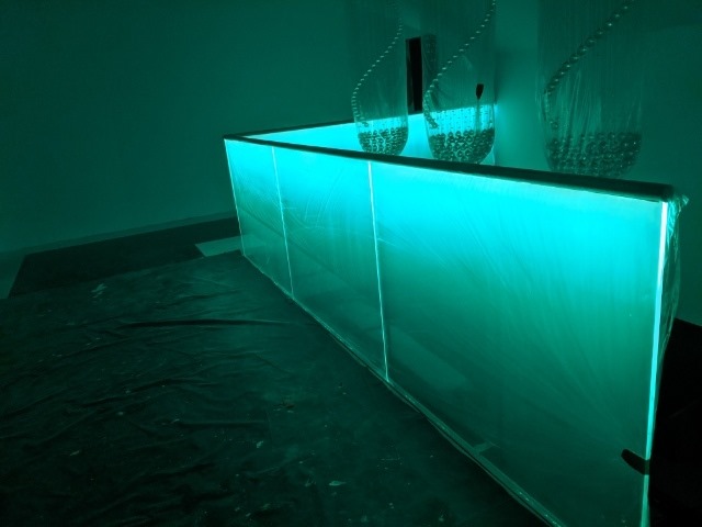 Podświetlana na zielono ściana z paneli szklanych z dekoracyjnymi sznurami z koralikami na górze, zabezpieczona folią ochronną.