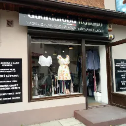 Fasada sklepu z odzieżą używaną 'Guardaroba Italiano' z wystawą manekin&oacute;w w oknie prezentujących białą bluzkę i szarą sp&oacute;dnicę oraz sukienkę w kwiaty, tablicą informującą o dostawach i godzinach...